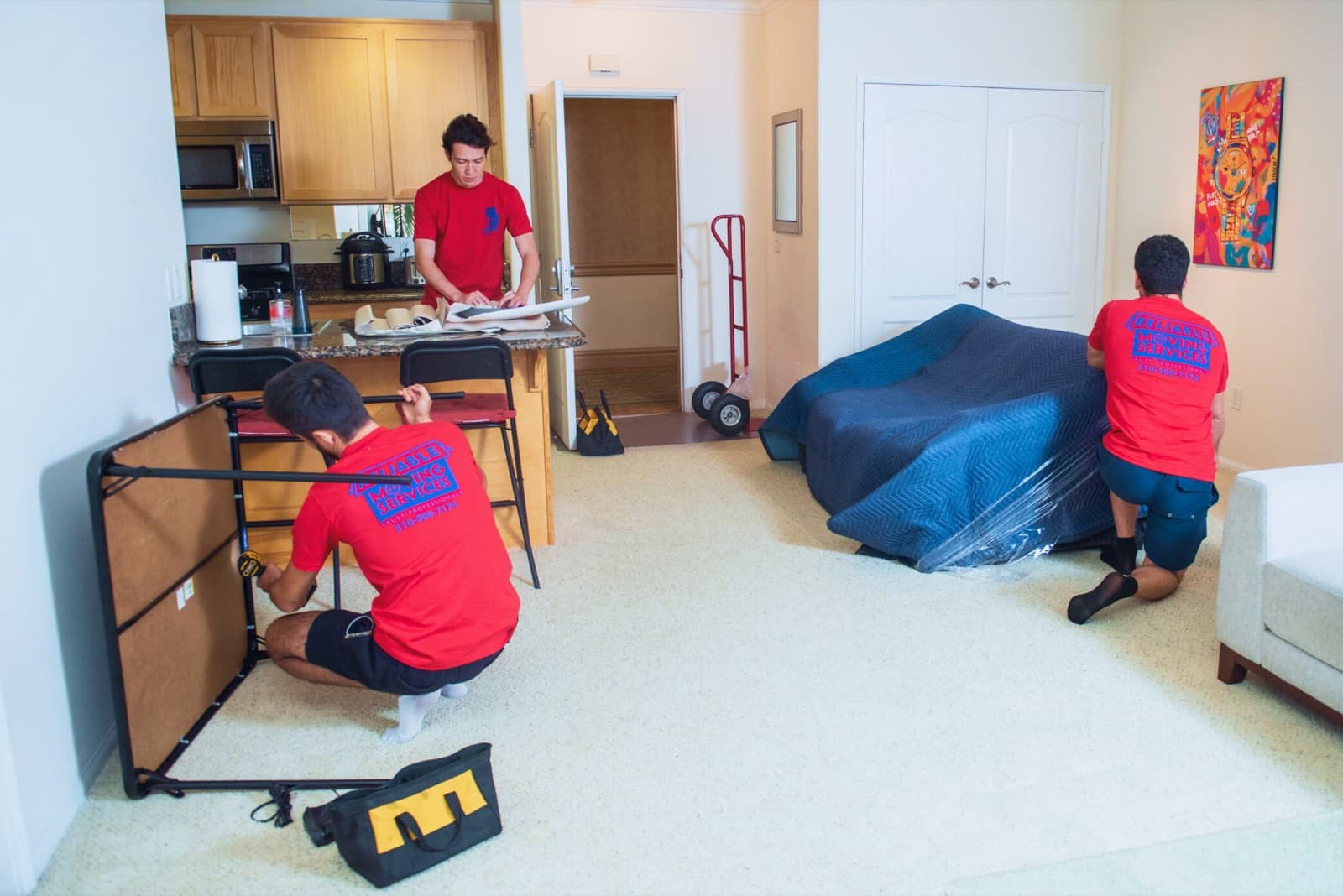 Crew disassembling a bed frame while a sofa waits wrapped in moving blankets