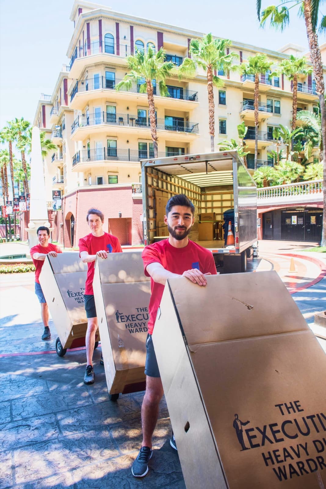 Movers rolling wardrobe boxes from the open truck